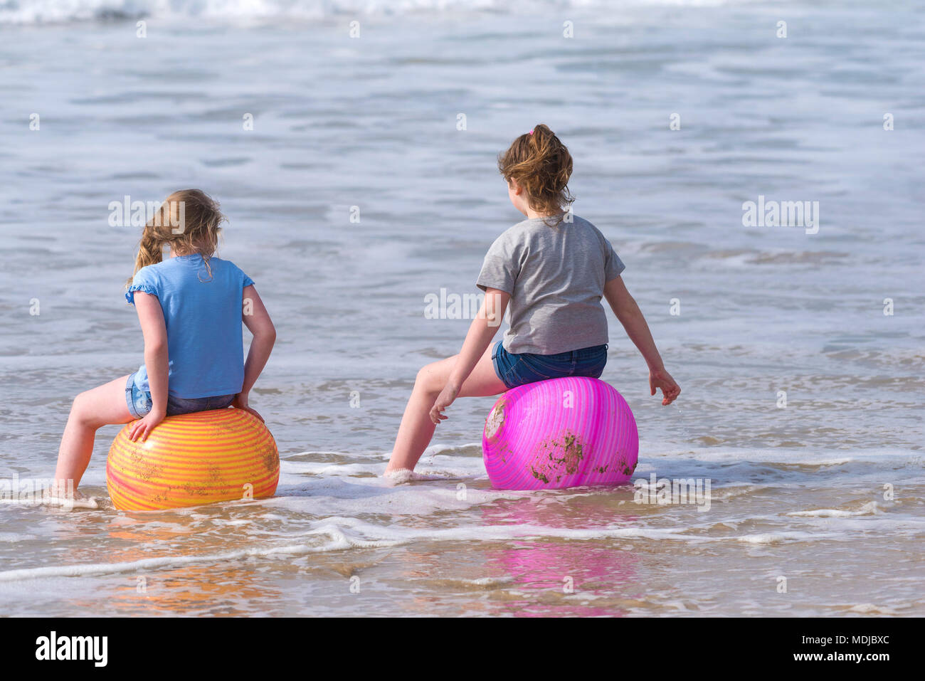 Les enfants en vacances se sont assis sur de grandes boules de plastique colorées dans la mer à Newquay Cornwall; Banque D'Images