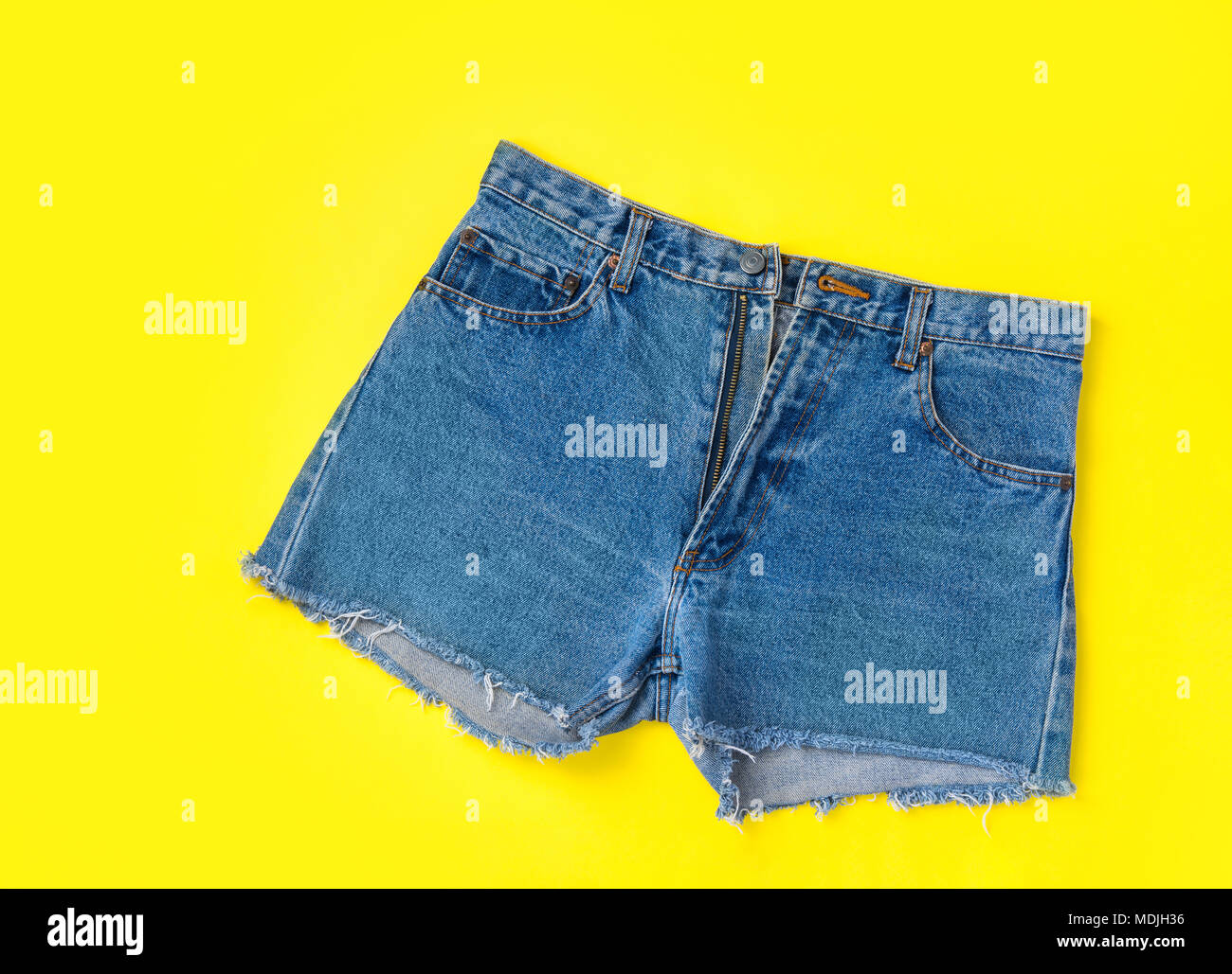 Les femmes à la mode classique Jeans denim shorts à franges sur fond jaune vif. Mise à plat. Street Summer Mode de vie Vente Voyage Vacances d'hiver Banque D'Images