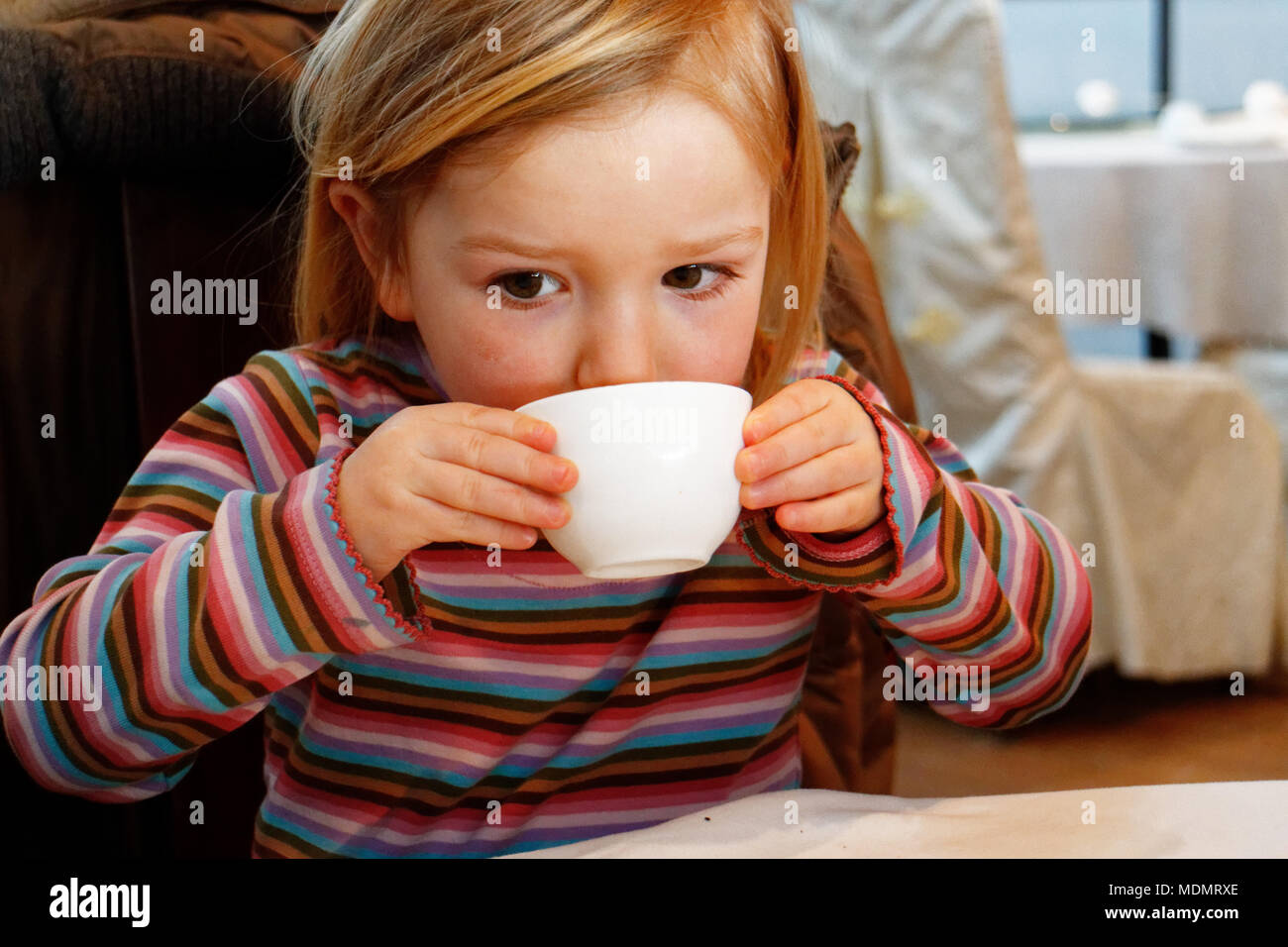 Une petite fille (3 ans) boire du thé vert d'une tasse de thé dans un restaurant chinois Banque D'Images