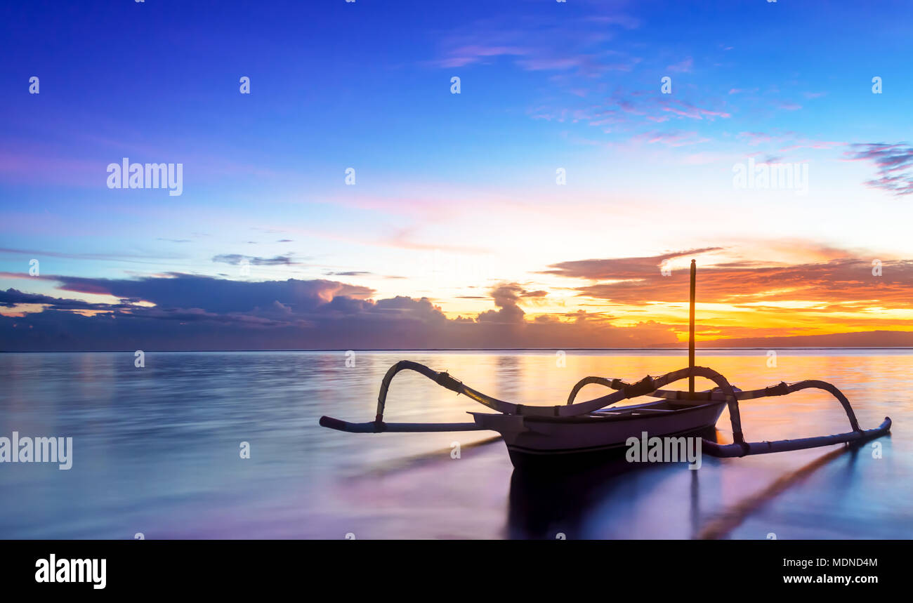 Jukung bali traditionnel bateau de pêche sur le lever du soleil près de la plage de sanur, face à l'océan. Le style traditionnel canot est équipé de deux bamboo Banque D'Images