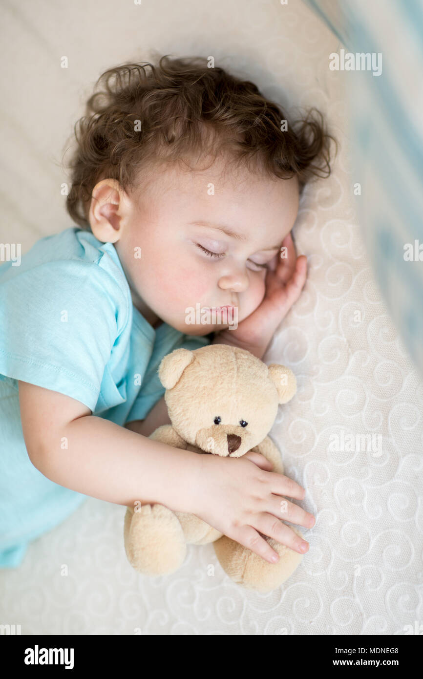 Adorable baby sleeping in bed, holding a teddy bear. Banque D'Images