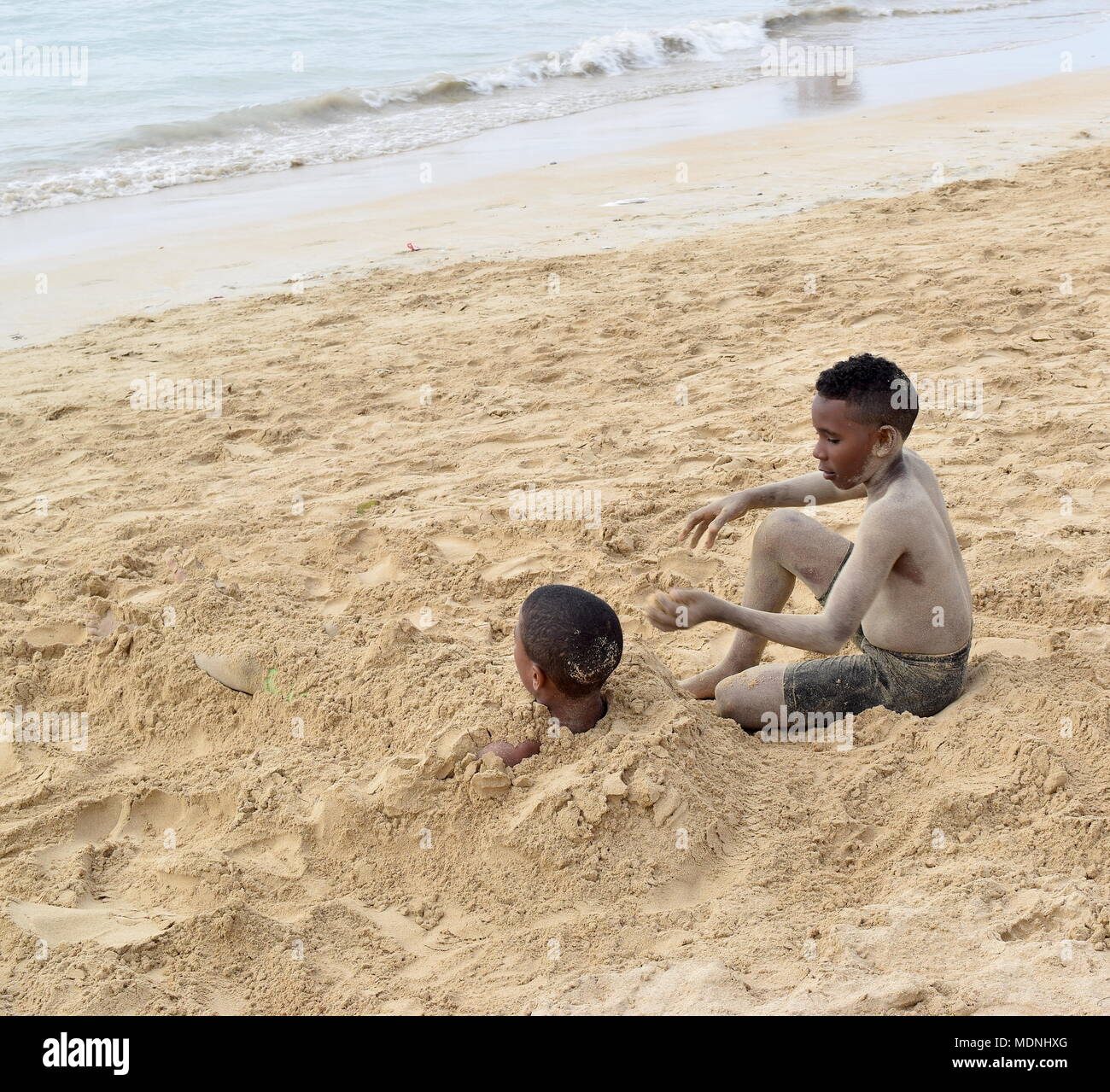 Les garçons couvrant l'un l'autre avec du sable sur la plage Banque D'Images