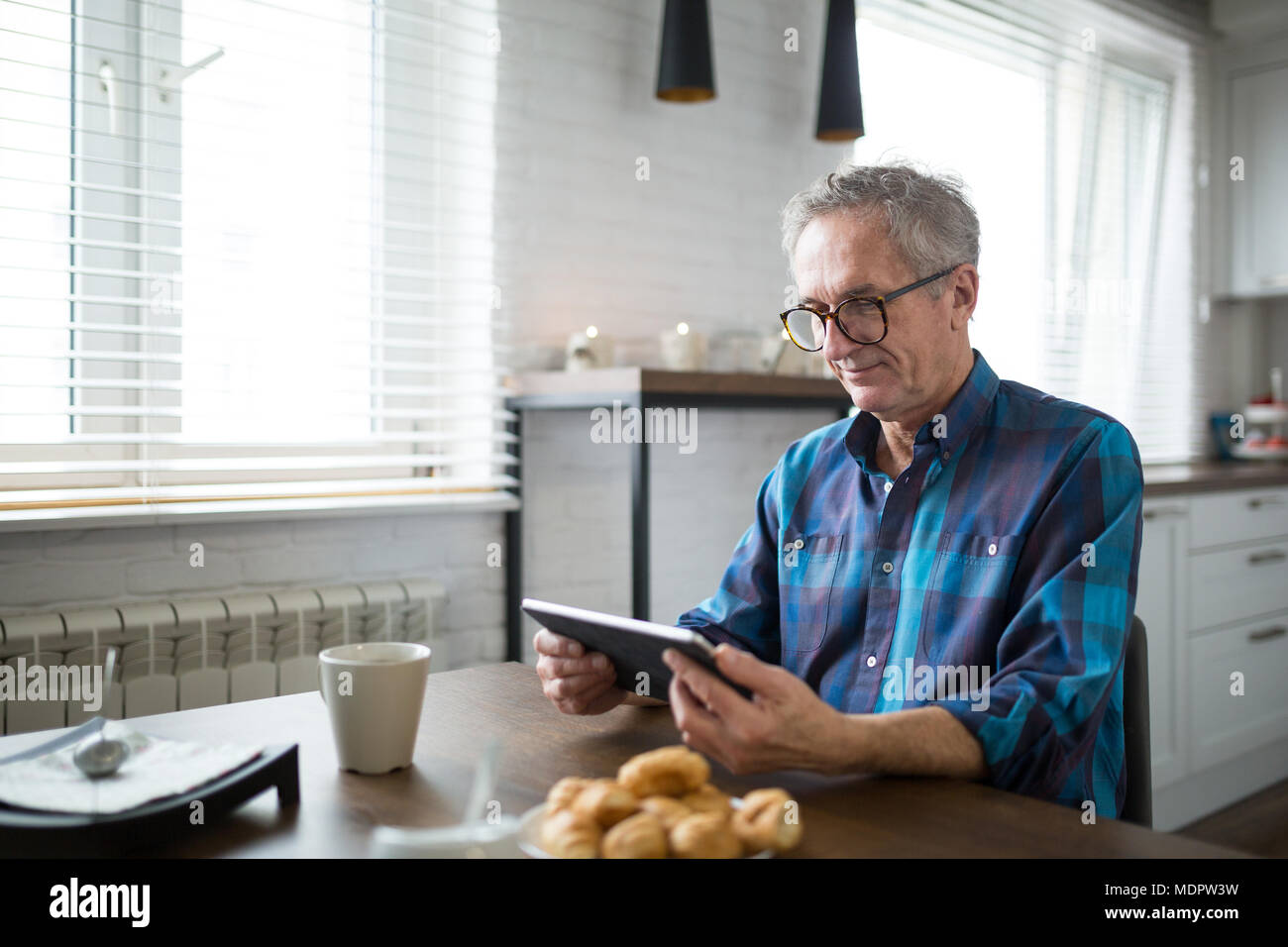 Portrait de côté heureux senior man reading ebook dans la cuisine Banque D'Images