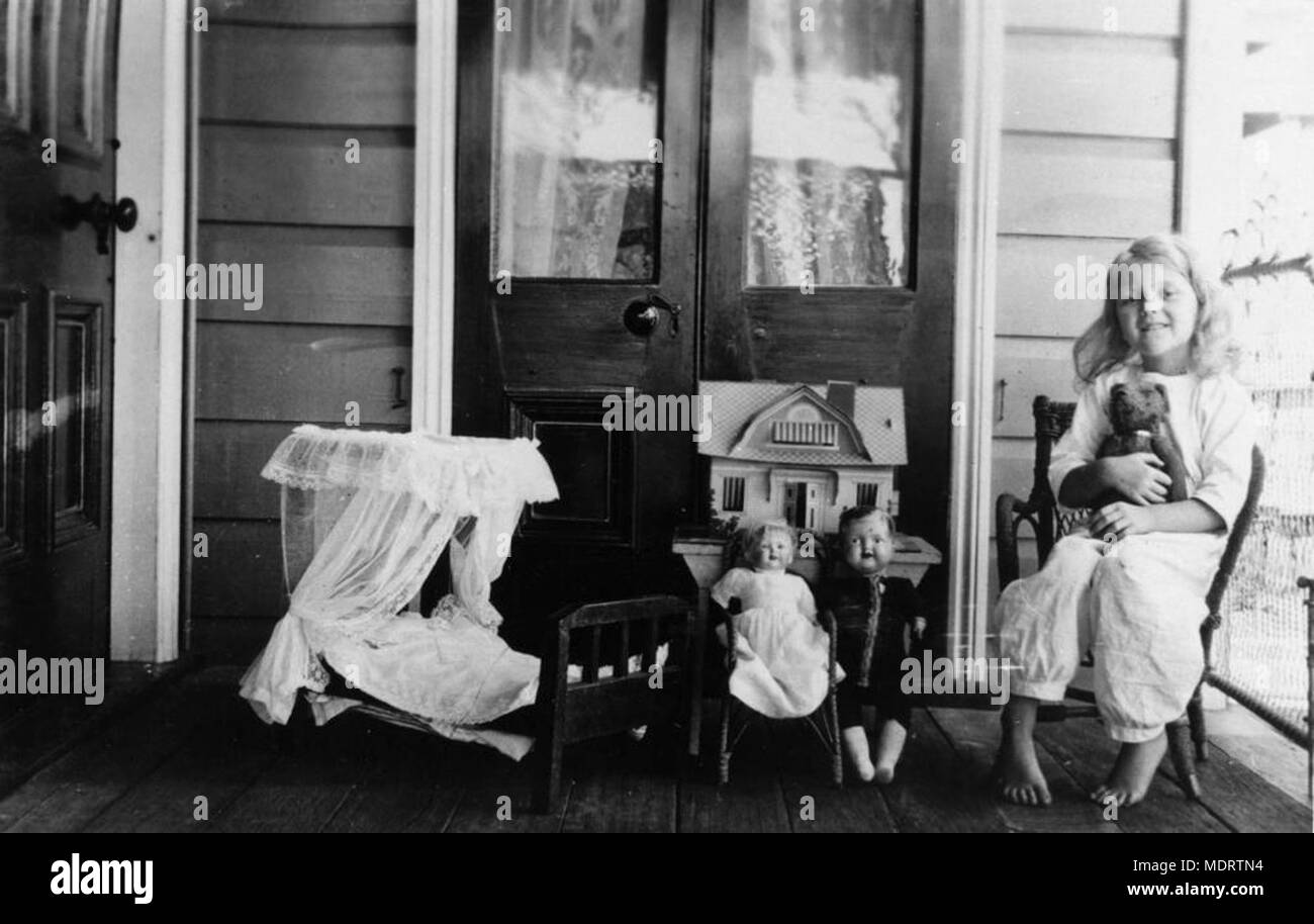 Enfant jouant avec ses poupées sur la véranda de son. Emplacement : Kangaroo Point, Brisbane Description : Jeune fille, probablement un membre de la famille Hartshorn, jouant sur la véranda avec ses poupées, ours, maison de poupées et de petits lit bébé. Banque D'Images
