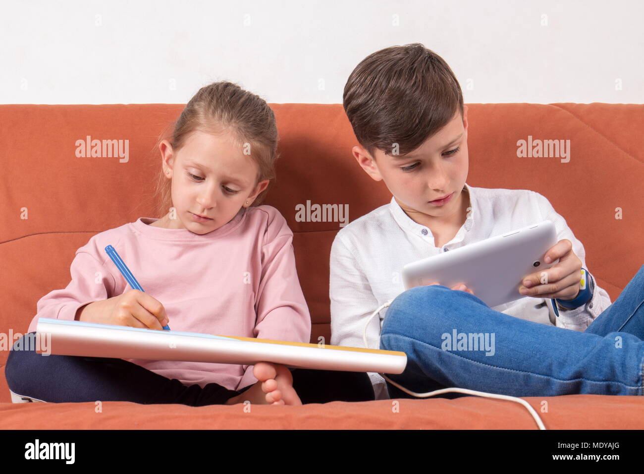 Deux enfants qui jouent, un avec le livre à colorier et les autres avec la tablette numérique Banque D'Images