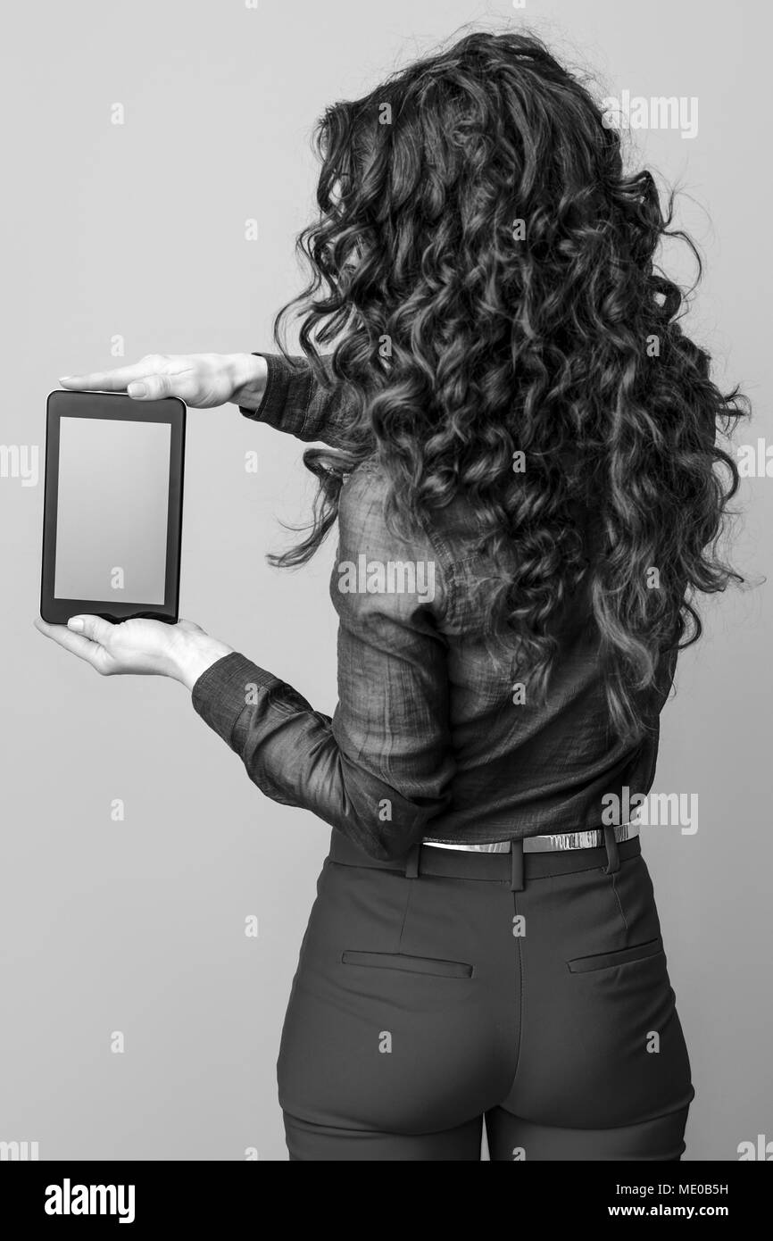 Vu de dos trendy femme aux longs cheveux brun ondulé montrant tablet PC écran blanc isolé sur Banque D'Images