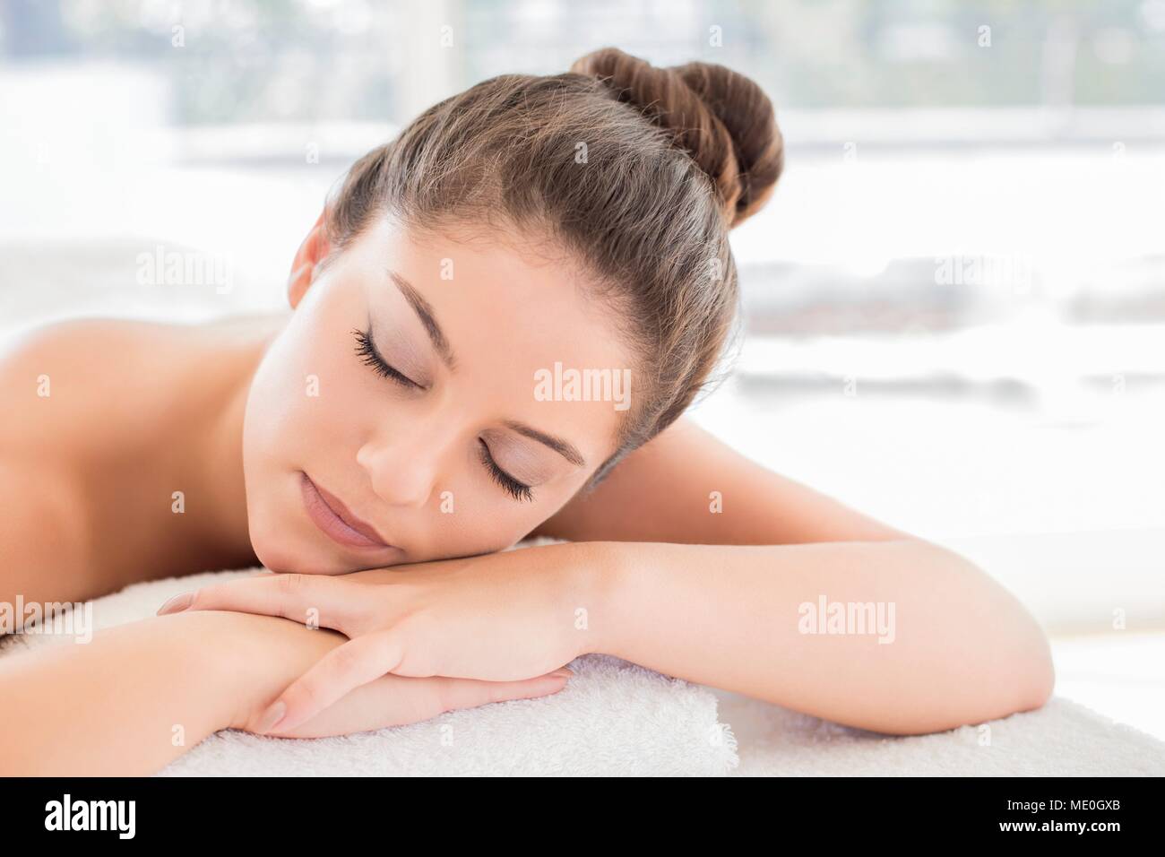 Jeune femme allongée sur une serviette dans un bain, les yeux fermés. Banque D'Images