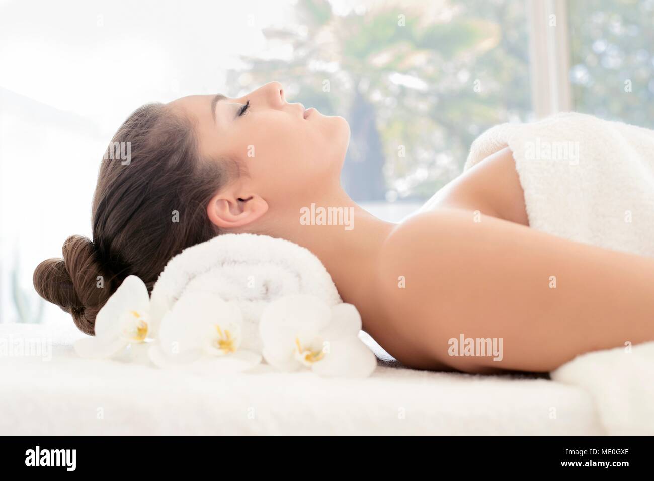 Jeune femme allongée sur une serviette dans un bain, les yeux fermés. Banque D'Images
