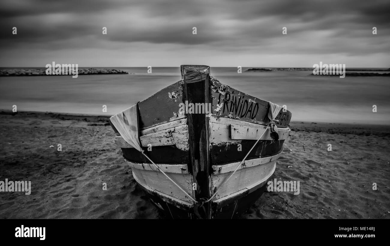 Une longue exposition d'un bateau sur une plage sous un ciel moody en Espagne. Banque D'Images