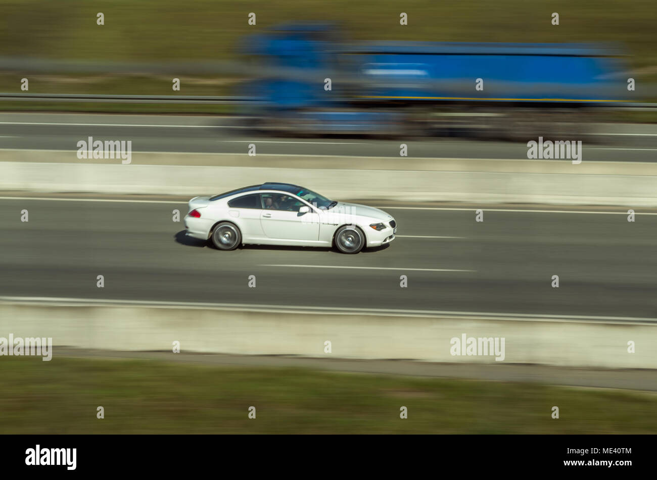 Puissant blanc coupé sport voiture sur l'autoroute avec motion gelée et camion bleu avec blurred motion. Zabrze, hautes terres de Silésie, Pologne. Banque D'Images