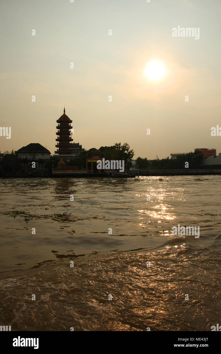 Silhouette d'un bâtiment traditionnel contre une pagode orange coucher de soleil sur la rivière Chao Phrya, Bangkok, Thaïlande. Banque D'Images