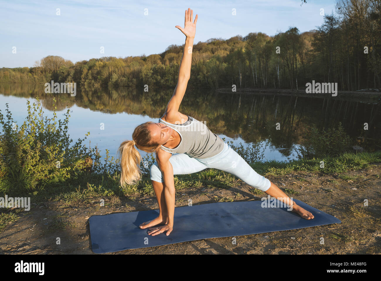 Young woman exercising yoga par le lac au coucher du soleil, les gens voyagent nature bien-être et détente concept. Tourné en France, en Europe. Banque D'Images