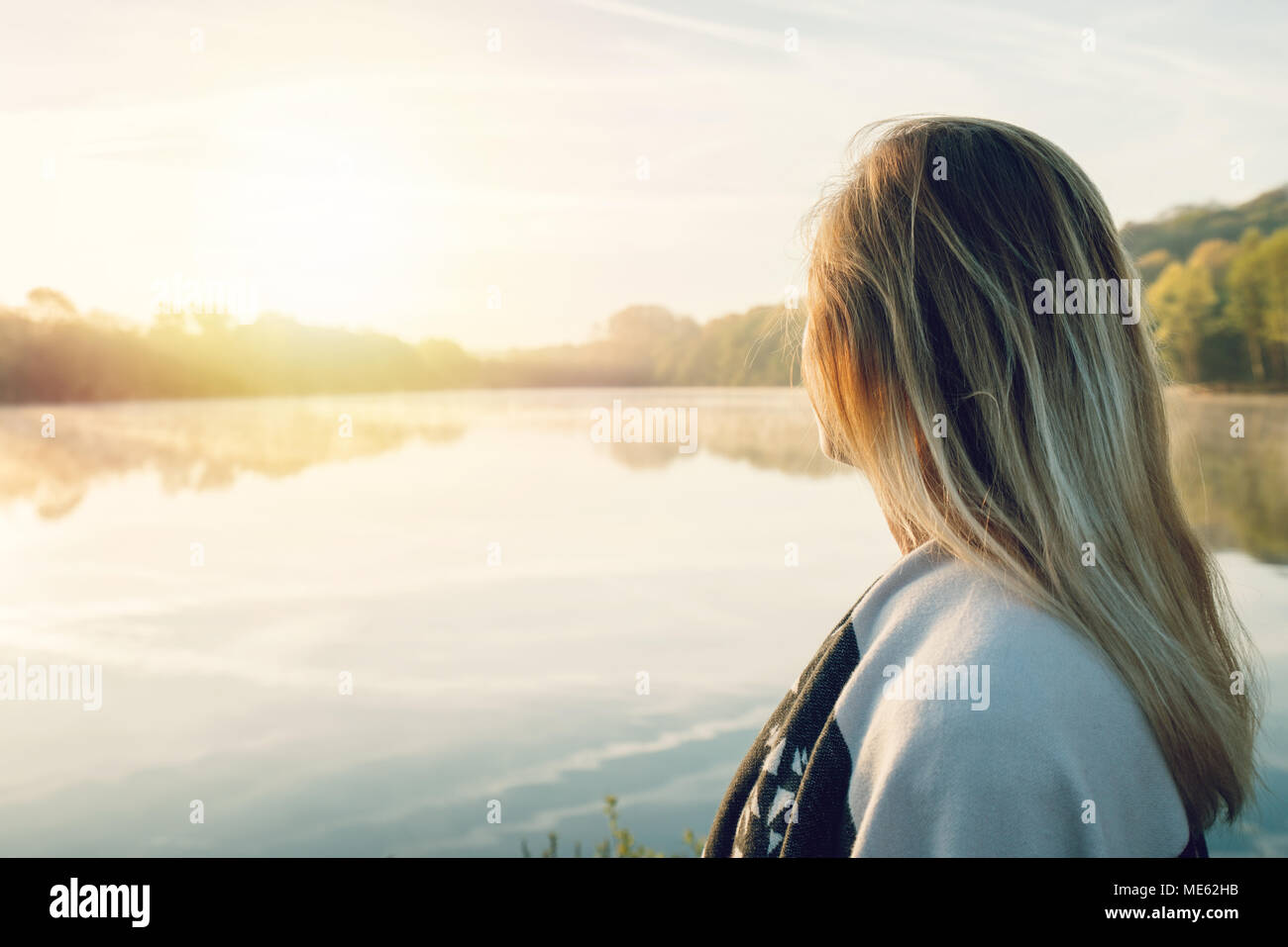 Jeune femme contemplant la nature par le lac au lever du soleil, le printemps, la France, l'Europe. Les gens voyagent de détente dans la nature concept. L'image des tonalités Banque D'Images