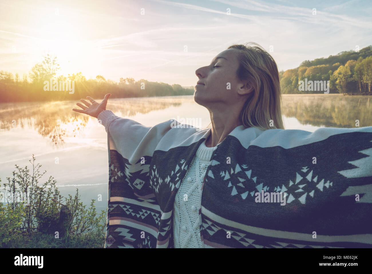 Jeune femme bras tendus par le lac au lever du soleil, jouissant de la liberté et de la vie, les gens voyagent bien-être concept. Tourné en France, en Europe. Banque D'Images