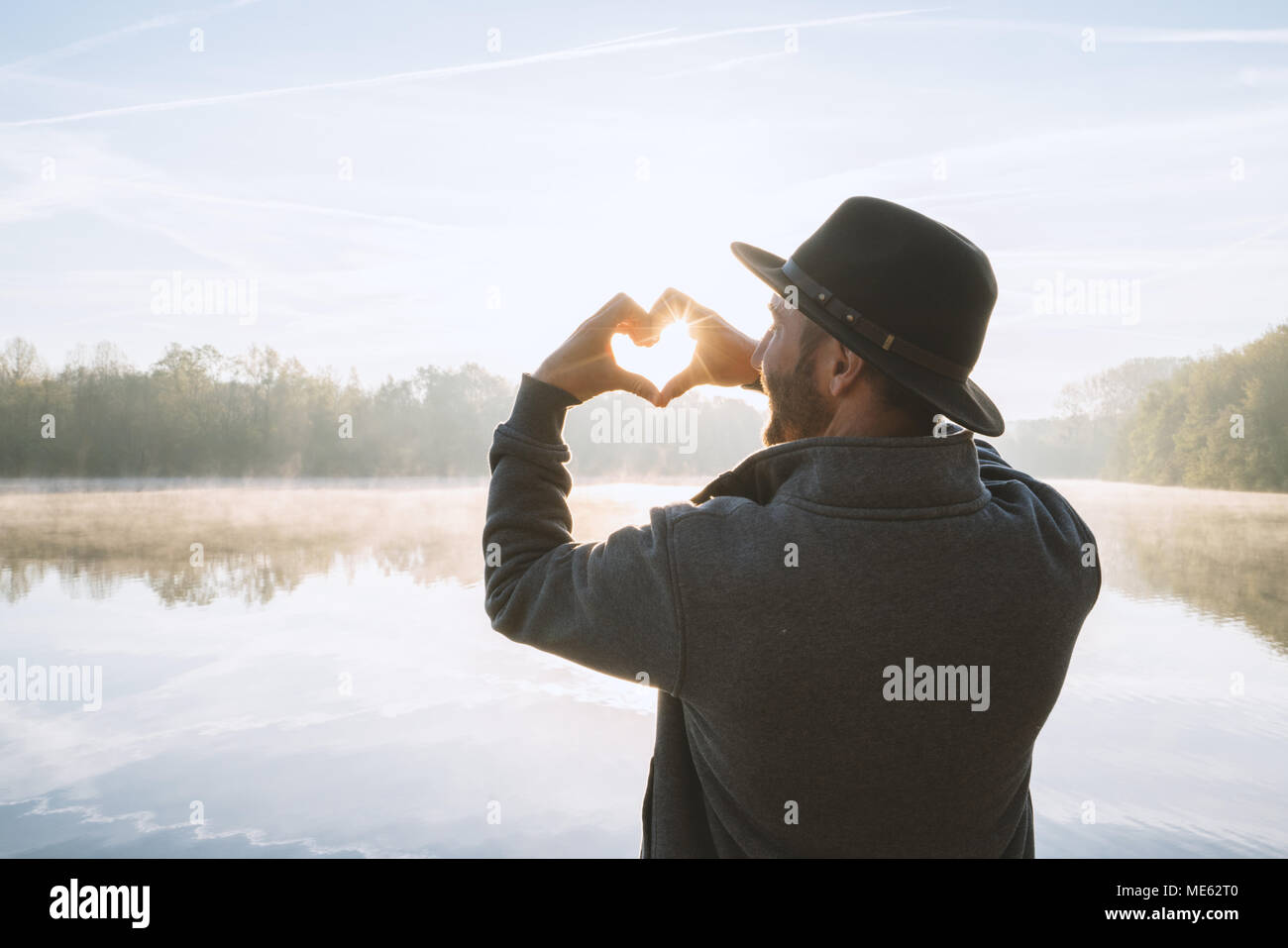 Jeune homme debout près du lac au lever du soleil en forme de coeur collés sur le beau paysage, la réflexion sur l'eau. Les gens aiment voyager Banque D'Images