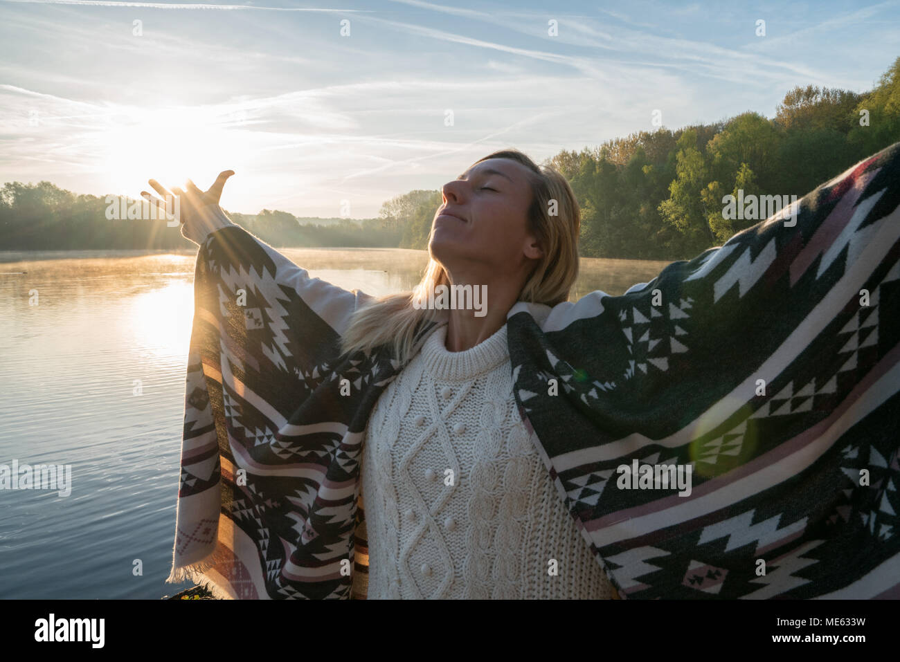 Jeune femme bras tendus par le lac au lever du soleil, jouissant de la liberté et de la vie, les gens voyagent bien-être concept. Tourné en France, en Europe. Banque D'Images