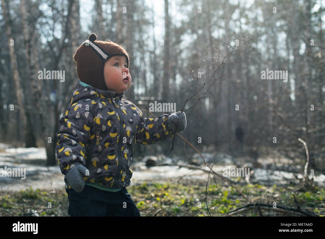 L'enfant joue émotionnellement avec une brindille, la magie et le charme de la forêt. Sans les feuilles de la forêt au printemps ou en automne. Banque D'Images