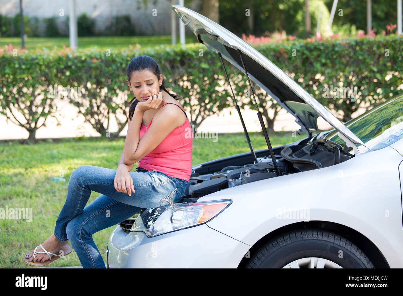 Closeup portrait, jeune femme en rose tanktop des ennuis avec sa voiture cassée, assis sur le capot ouvert, inquiets du moteur vert des arbres et des arbustes isolés Banque D'Images