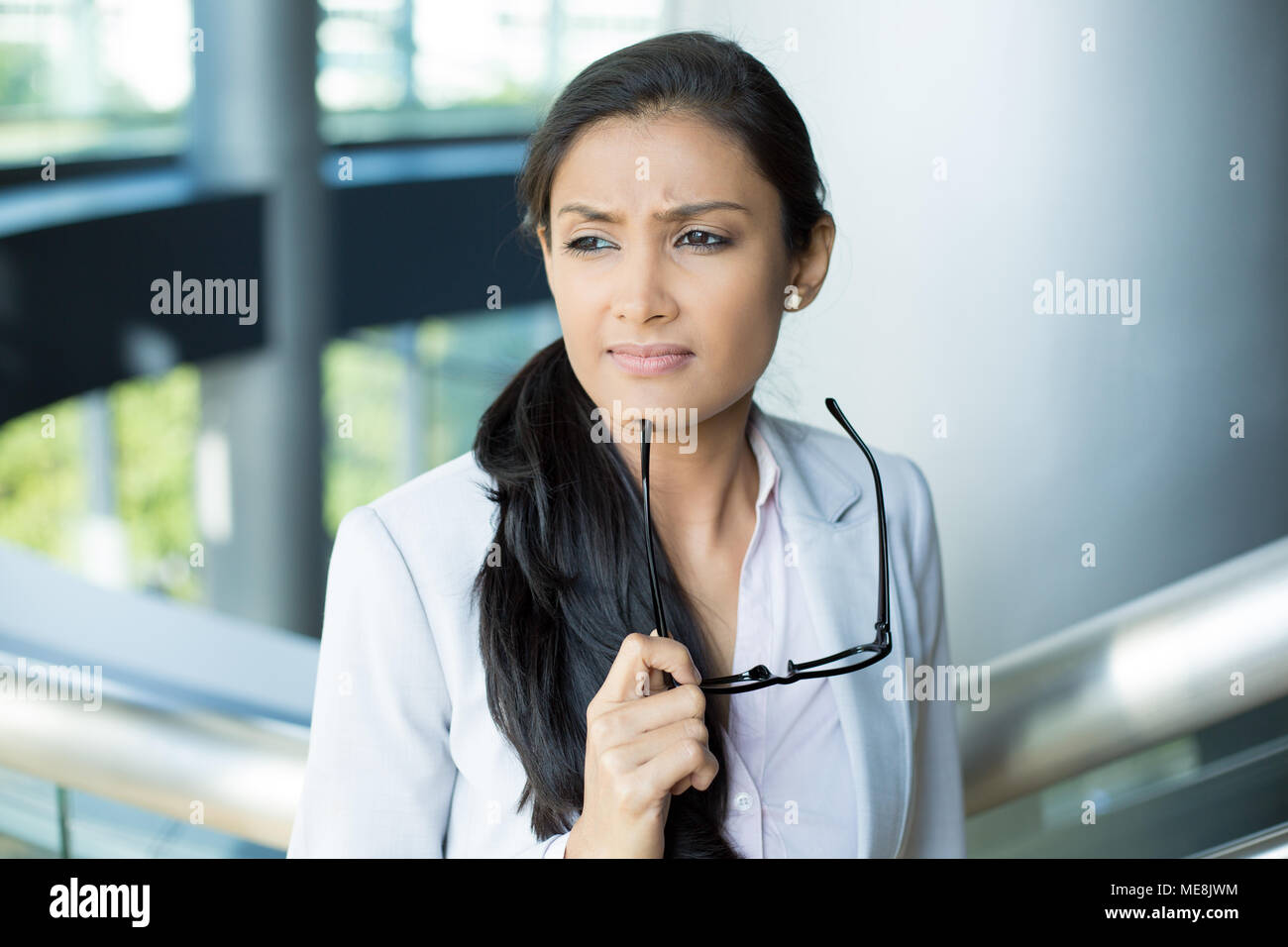 Closeup portrait, femme leader en costume gris avec des lunettes noires sous le menton en réfléchissant, cogitative, nécessitant de prendre des décisions difficiles, isolées à l'intérieur Banque D'Images