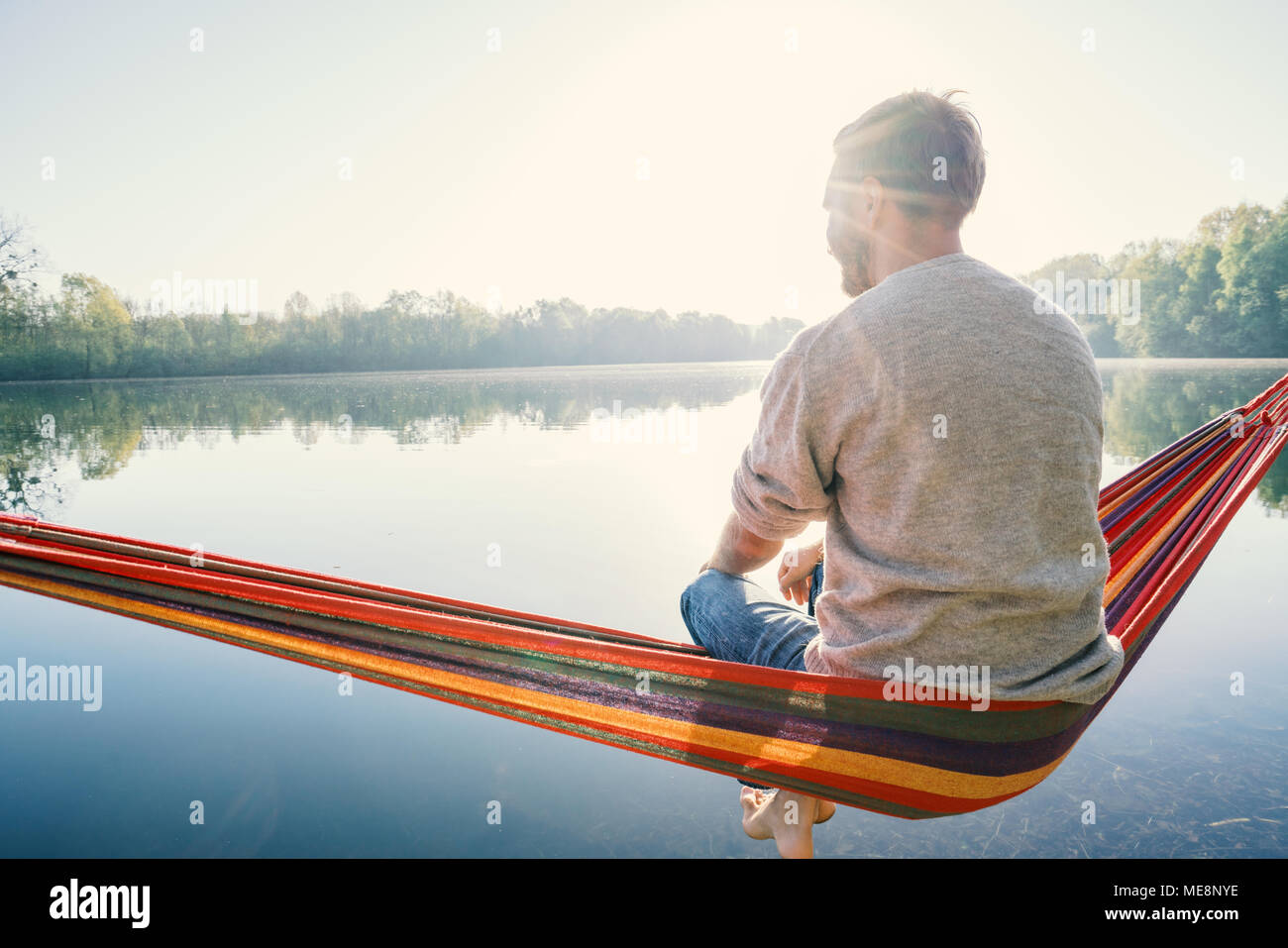 Jeune homme sur hamac détente au bord de la lac dans le matin, la lumière du soleil. Les gens voyagent bien-être la paresse concept. France, Europe Banque D'Images