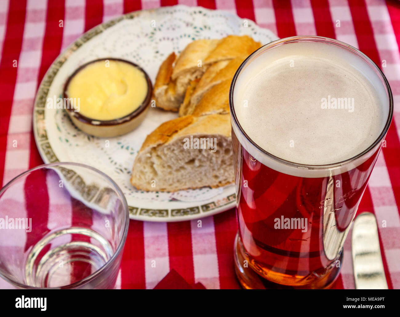 Repas dans un pub typique de la buvette : une pinte de bière dans un verre recto verso avec pain et beurre rouge et blanc sur une nappe vichy vérifié Banque D'Images