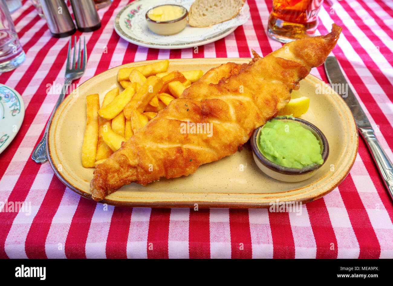 Poisson battues (bière batter), Golden Chips, petits pois déjeuner ou dîner : plaque de pub anglais traditionnel de la nourriture sur une case rouge et blanc nappe Vichy Banque D'Images