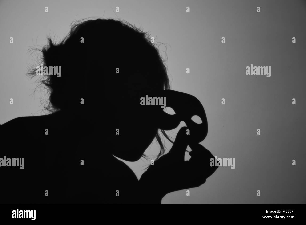 Une photographie noir et blanc représentant l'ombre d'une femme tenant un masque. Banque D'Images