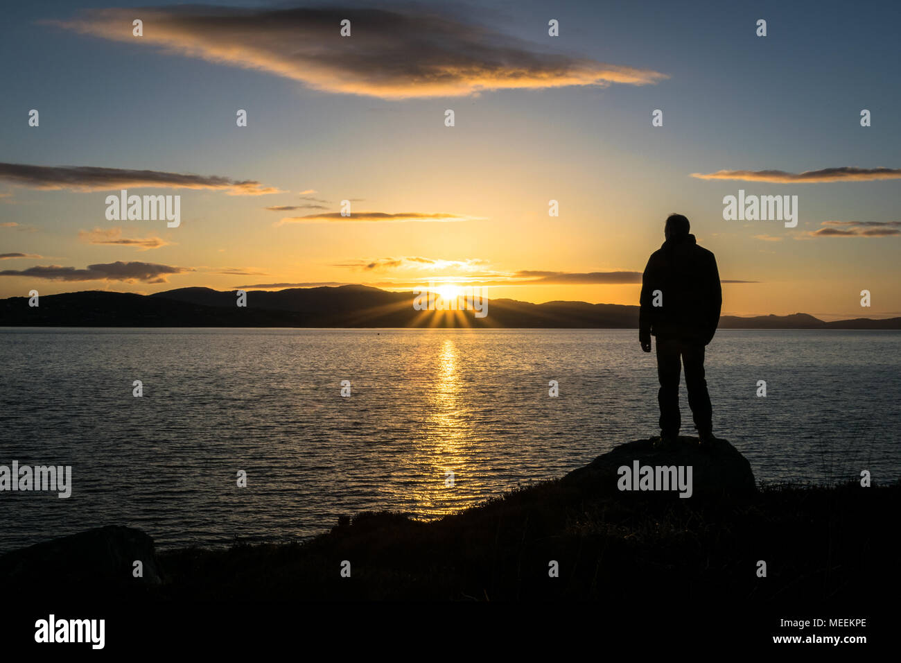C'est la silhouette d'une personne regardant le soleil se coucher derrière des montagnes à la mer. Cette photo a été prise près de l'Irlande Buncrana Banque D'Images