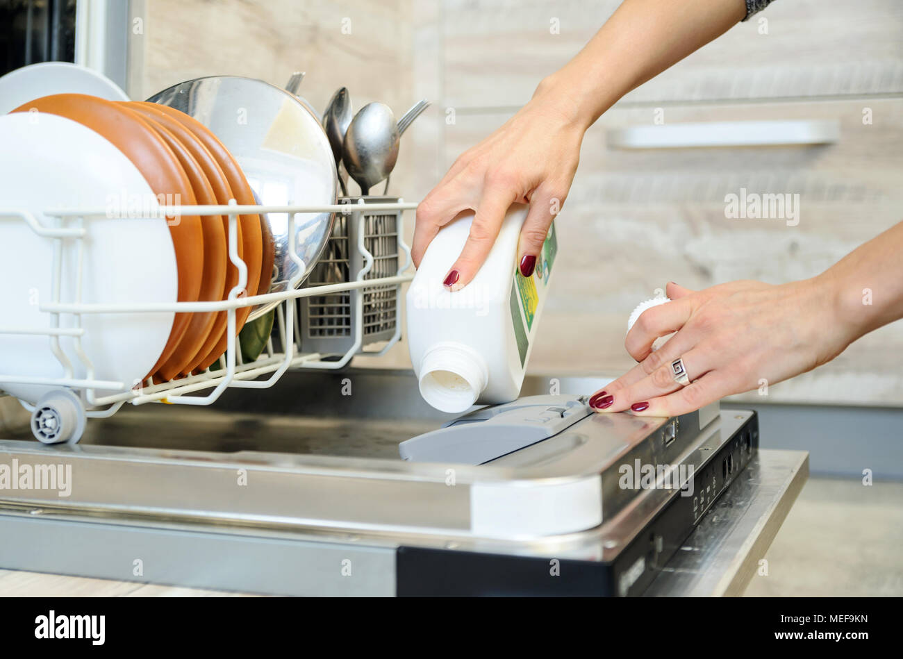Le woman's hand holding une bouteille de détergent et l'ajoute au lave-vaisselle. Banque D'Images