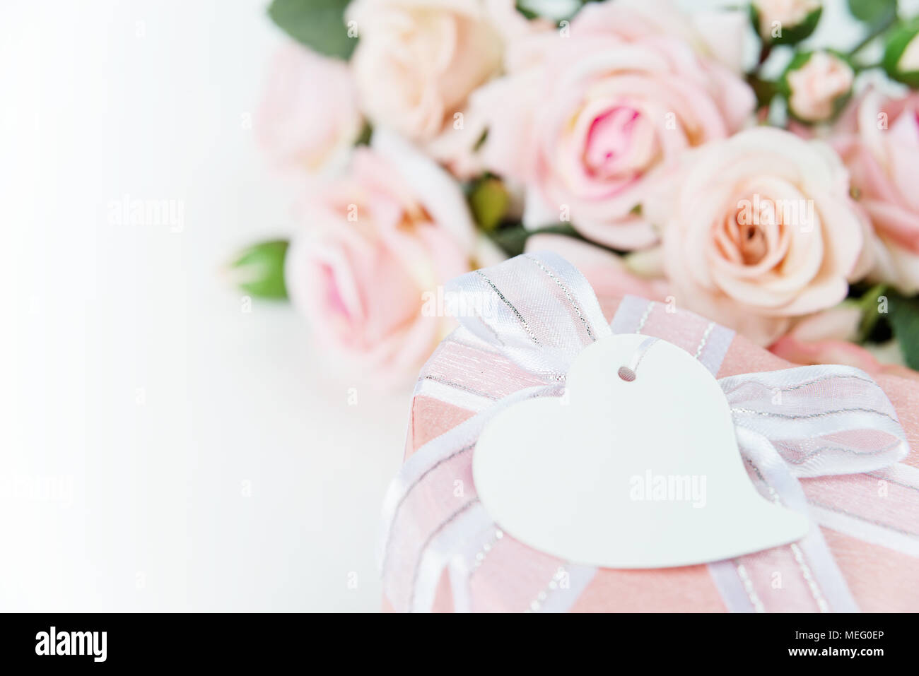Boîte-cadeau avec étiquette, ruban et fleurs rose rose sur un fond clair Banque D'Images