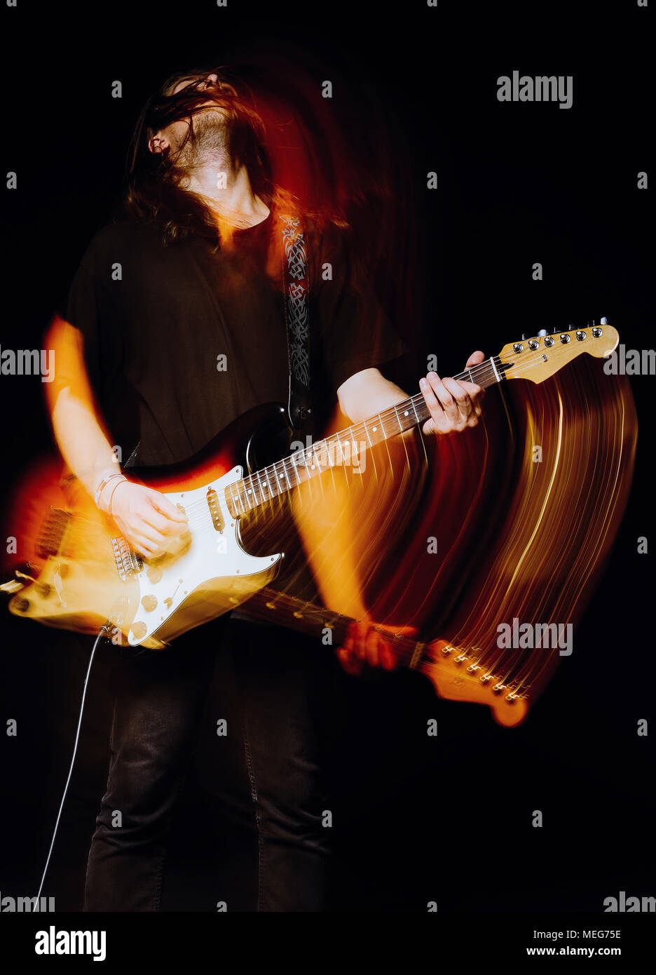 Studio portrait : un beau jeune homme musicien (rock) avec des cheveux longs à jouer de la guitare électrique. L'effet flou (motion) Banque D'Images