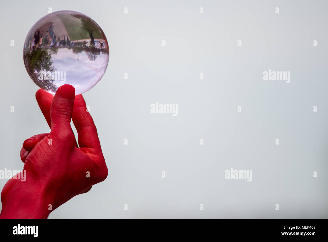 Homme avec les mains rouges habillé comme le diable est titulaire et joue avec une boule de cristal de verre isolé contenant des réflexions de personnes Banque D'Images