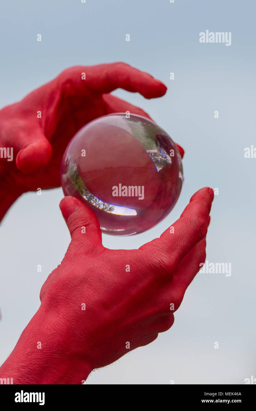Homme avec les mains rouges habillé comme le diable est titulaire et joue avec une boule de cristal de verre isolé contenant des réflexions de personnes Banque D'Images