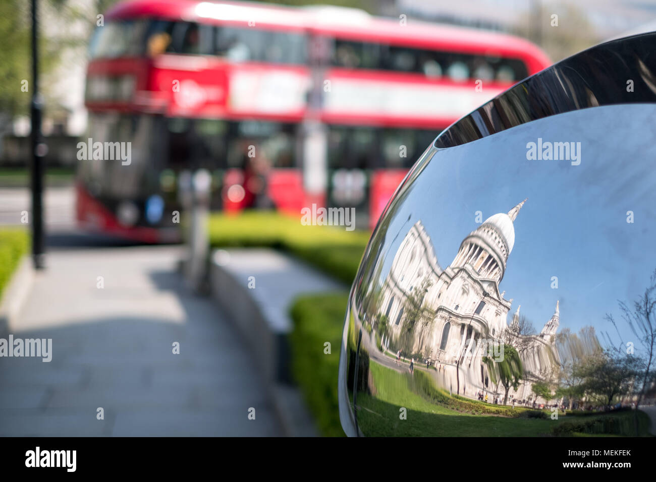 Reflet déformé de la Cathédrale St Paul, London UK, reflétée dans la surface en métal brillant miroir de sculpture, blurred bus rouge à l'arrière-plan. Banque D'Images