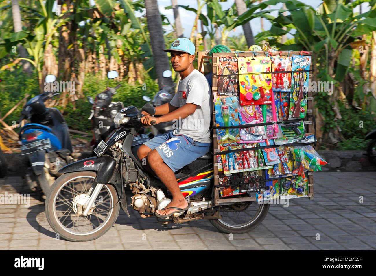 Vendeur de rue Mobile, transportant ses marchandises des jouets pour enfants en plastique à l'arrière de sa moto. Lovina, Bali, Indonésie Banque D'Images