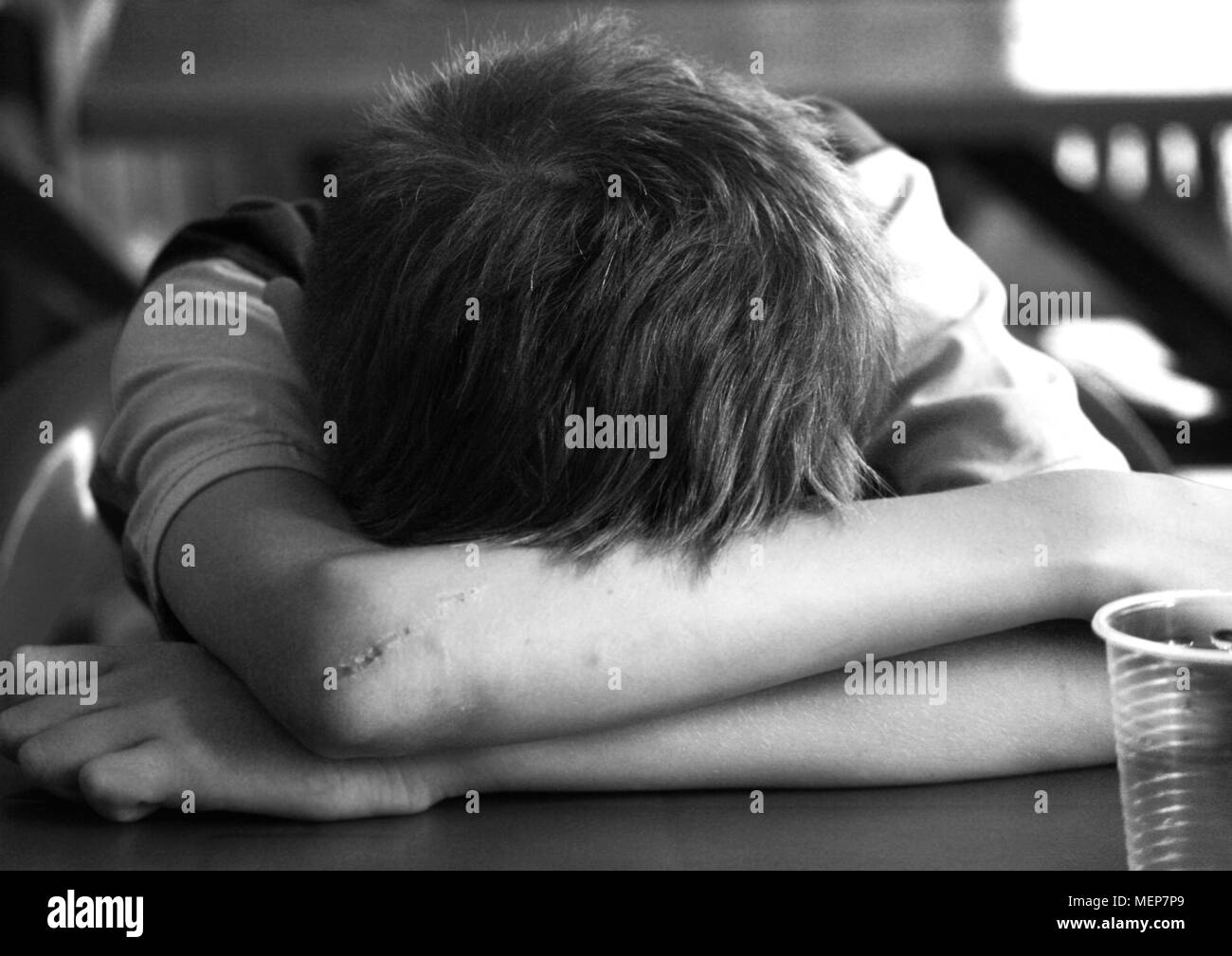 Photo en noir et blanc d'un adolescent difficile. Il dort dans un café à côté d'un verre vide, ses mains dans les plaies. Banque D'Images