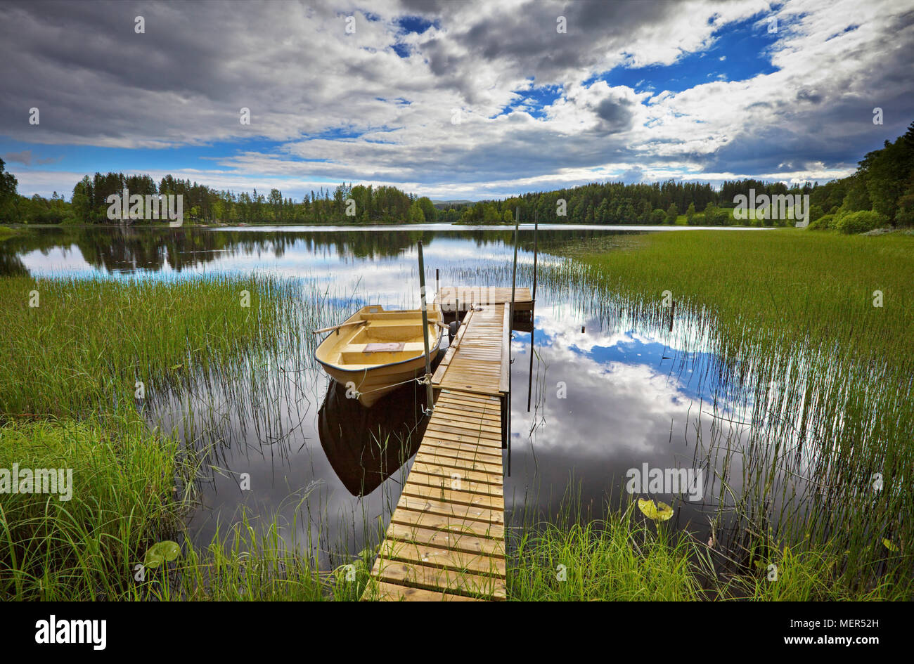 Un bateau à rames est amarré à une jetée dans un lac forêt vitreux Banque D'Images