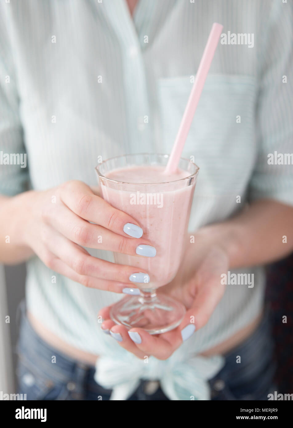 Une section d'une fille à la mode de porter des couleurs pastel et tenant un verre plein de smoothie aux fraises milkshake ou avec une paille rose Banque D'Images