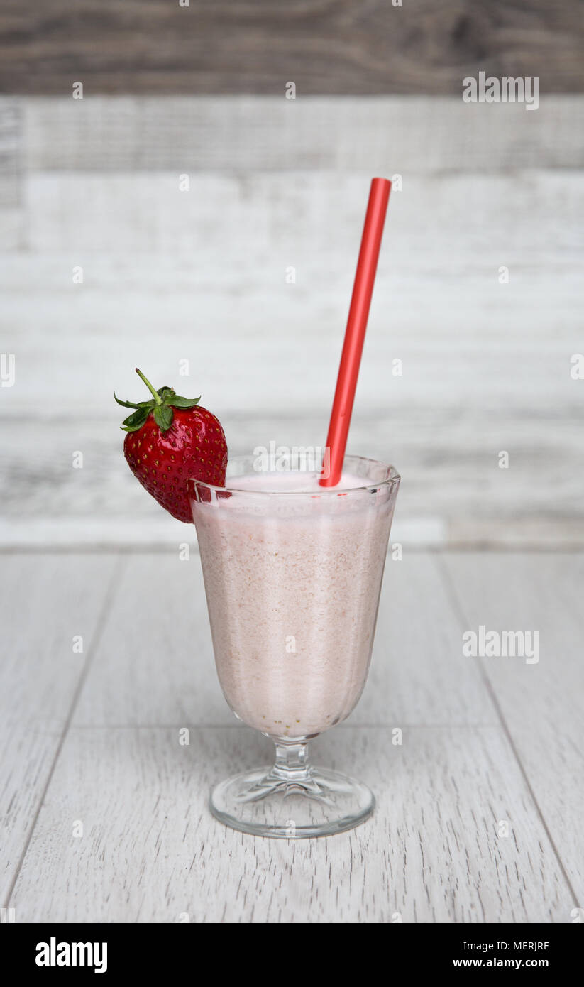 Un rose pastel strawberry milkshake smoothie ou dans un grand verre et décoré avec des fruits et une paille rouge sur un fond blanc. Banque D'Images