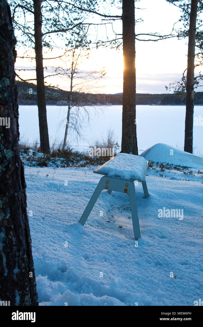 Un banc en bois est debout au bord d'un lac couvert de glace. Banque D'Images