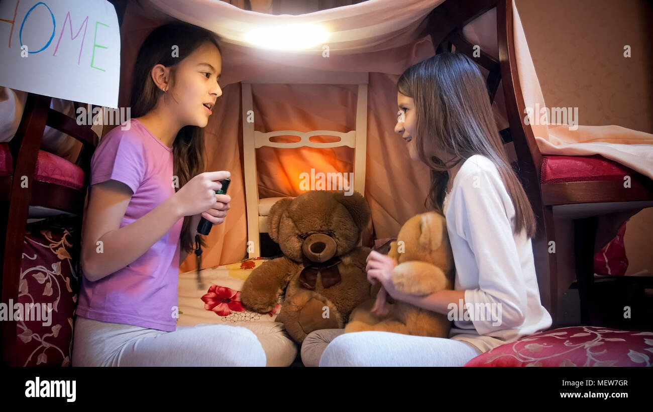 Deux jolies filles assis dans une tente faite de couvertures et de raconter des histoires. Banque D'Images
