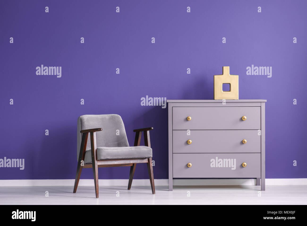 Fauteuil en bois gris à côté d'un mur violet violet contre l'armoire à l'intérieur salle de séjour minimal Banque D'Images