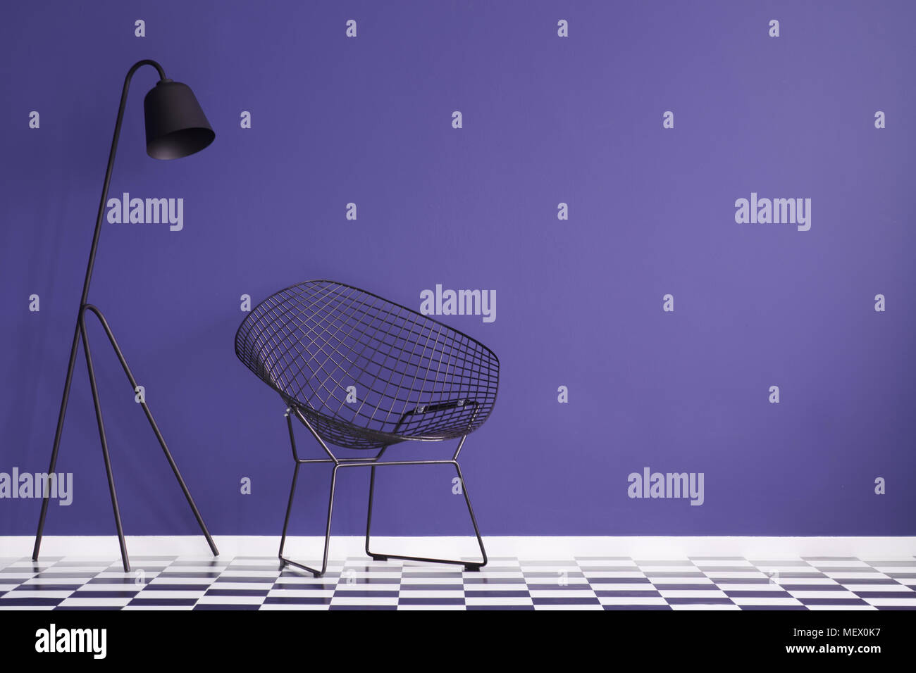 Lampe noire à côté d'un fauteuil sur le sol en damier à l'intérieur violet with copy space Banque D'Images