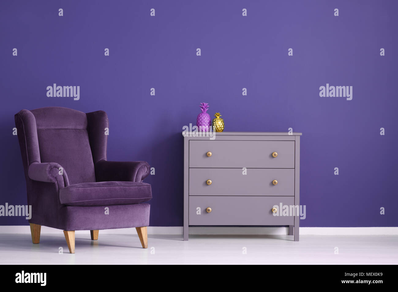 L'ananas sur l'or du cabinet violet à côté d'un fauteuil de velours pourpre dans le salon intérieur Banque D'Images