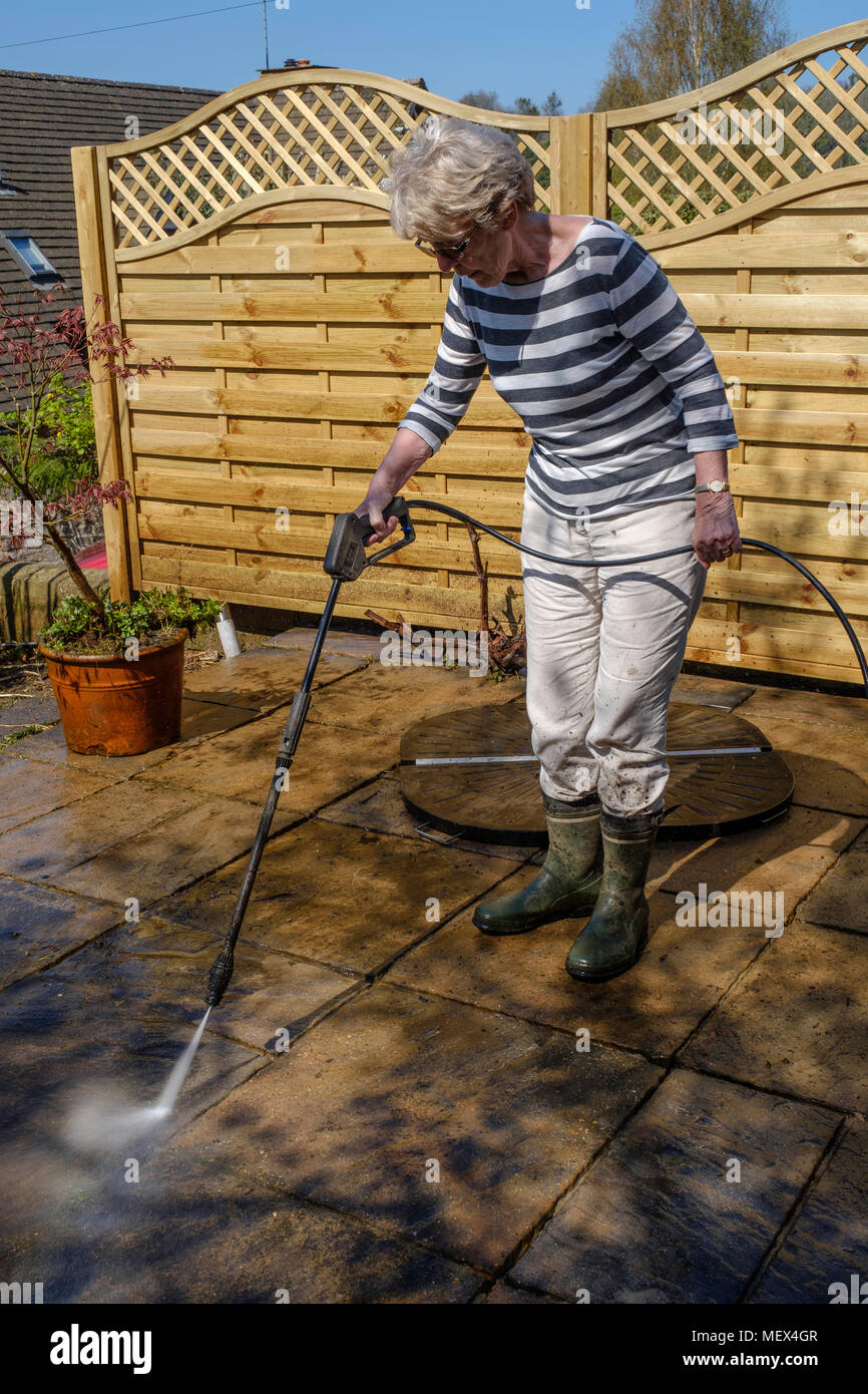 Femme plus âgée de nettoyage par aspersion PATIO avec la rondelle de pression sur jardin, Angleterre UKUK. Banque D'Images