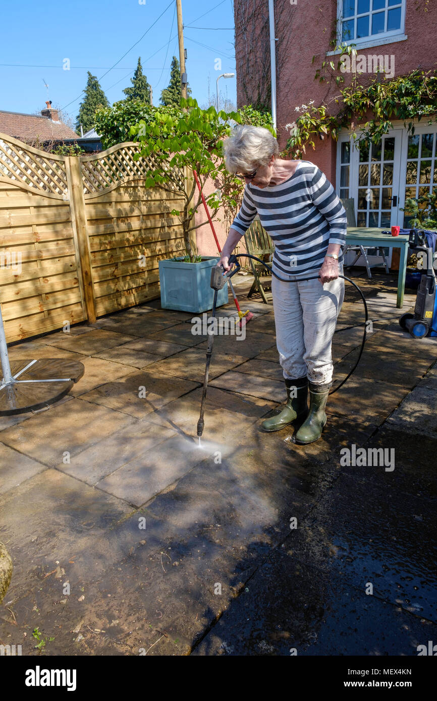 Femme plus âgée de nettoyage par aspersion PATIO avec la rondelle de pression sur jardin, Angleterre UKUK. Banque D'Images
