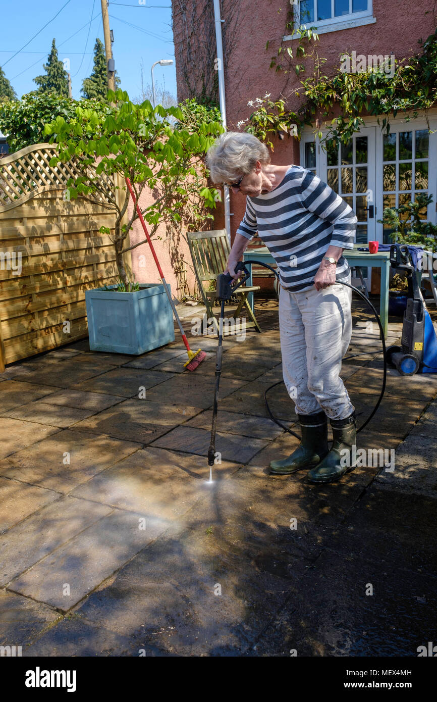 Femme plus âgée de nettoyage par aspersion PATIO avec la rondelle de pression sur jardin, Angleterre UKUK. Banque D'Images