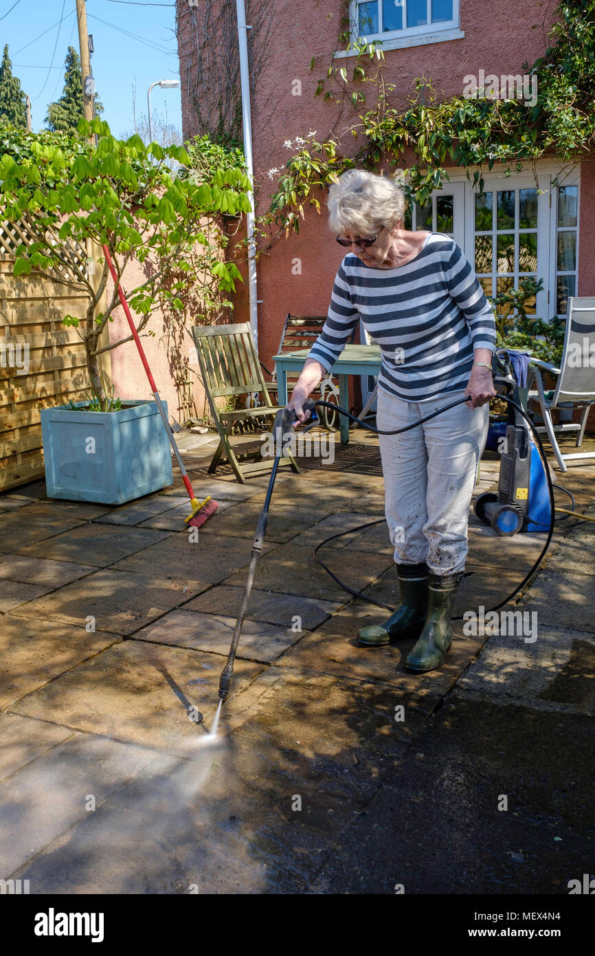 Femme plus âgée de nettoyage par aspersion PATIO avec la rondelle de pression sur jardin, Angleterre UKUK. Banque D'Images