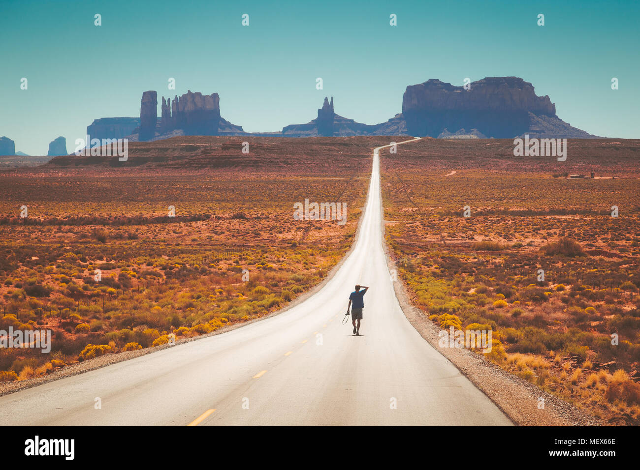 Classic vue panoramique de jeune homme marche sur célèbre Forrest Gump Road à Monument Valley à midi, de l'Utah, l'Ouest américain, USA Banque D'Images