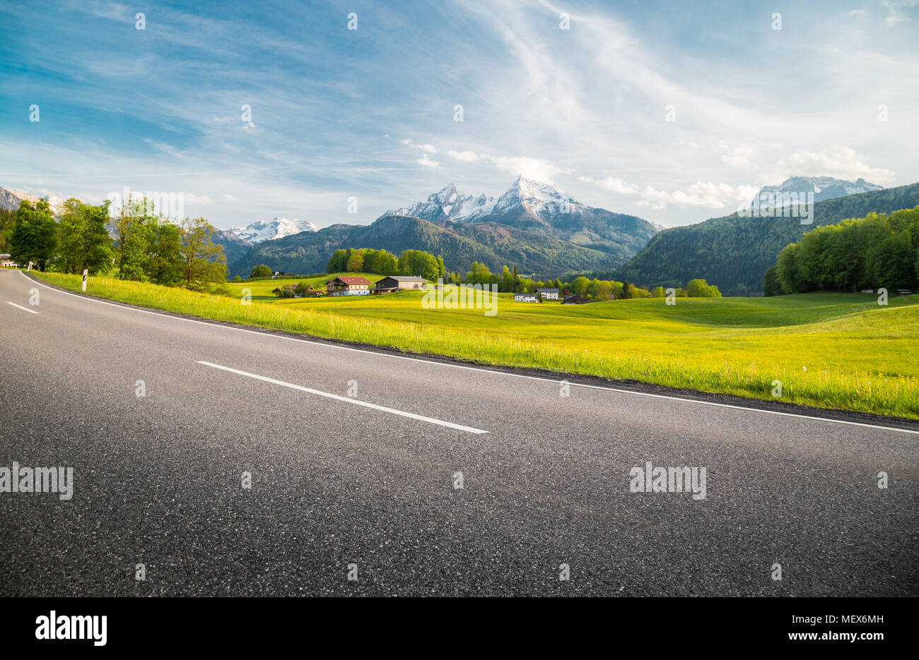 Vue panoramique de empty country road menant à travers les magnifiques paysages de montagne alpin avec des prés verts plein de fleurs au printemps Banque D'Images